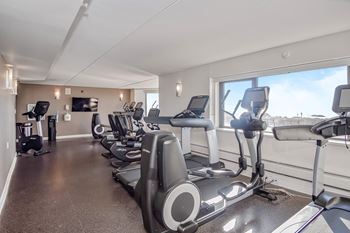 An exercise room with cardio equipment and a view of the city